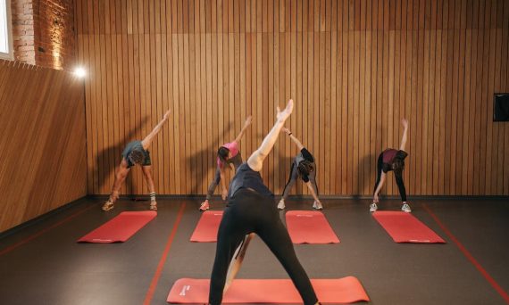 Yoga class with diverse adults stretching on mats in a cozy wooden studio.