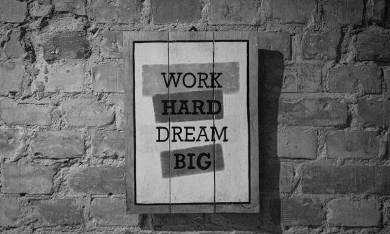 Black and white frame with inspirational Work Hard Dream Big inscription hanging on brick wall